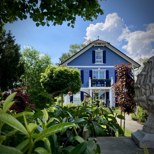 Ein blaues Haus mit wei&szlig;en Fensterl&auml;den hinter einem Garten